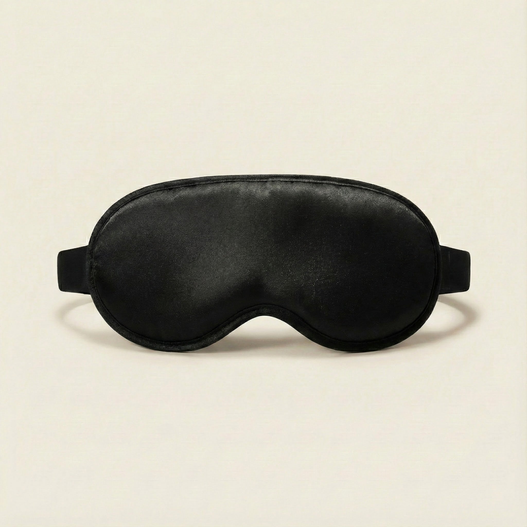 Black satin sleep mask on a beige background