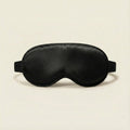 Black satin sleep mask on a beige background