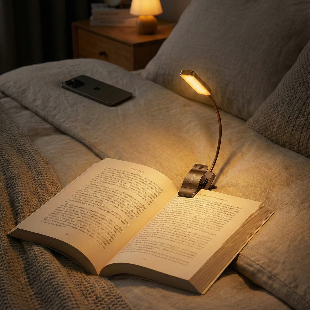 Open book with a lamp on a bed, next to a phone